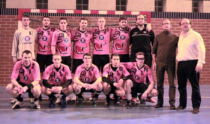 Photo d'équipe des seniors en maillot rose à motif de tigre, devant un but, avec deux dirigeants à droite