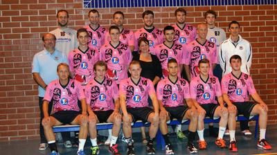 Photo d'équipe : les joueurs en maillot rose sur deux rangées devant un mur de briques, avec les dirigeants